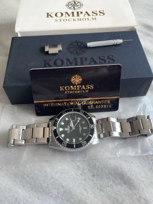 KOMPASS Stockholm silverfärgad klocka - Stilren klocka från KOMPASS Stockholm med silverfärgad länk i metall och svart urtavla. Klockan har tydliga markeringar, datumvisning och vridbar bezel. Perfekt accessoar för dig som gillar klassisk och tidlös design. Pris går att diskutera 