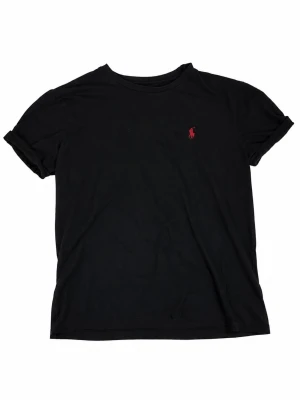 Ralph Lauren svart T-shirt - 🖤 Klassisk svart Ralph Lauren T-shirt med ikonisk röd broderad Pony-logga på bröstet.  Väldigt clean och tidlös modell som passar till allt – jeans, shorts, overshirt eller under en zip-up. Den svarta färgen tillsammans med den röda loggan ger en riktigt snygg kontrast.  ✨ Klassisk Ralph Lauren-design 🐎 Broderad röd Pony-logo 🖤 Svart färg 👕 Kortärmad / crewneck 👌 Enkelt och stilrent basplagg 📦 Skickas snabbt och välpaketerat 💬 Skriv gärna för mått eller fler bilder 🛍️ Fler märkesplagg finns på pr