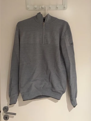 Quarter-zip Oscar Jacobson - Grå quarter-zip ifrån Oscar Jacobson med logga på vänster arm. Skrynklig då den inte använts på länge, mycket gott skick, inga skador/fläckar. Vadderad inuti. 