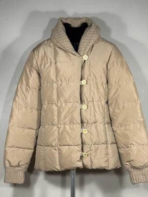 Escada Beige quilted puffer jacket with ribbed collar and cuffs - Stilren beige quiltad pufferjacka från Escada med stora knappar framtill och ribbstickad krage samt muddar vid ärmsluten. Jackan har en avslappnad passform och är perfekt för höst och vinter. Passar både till vardags och mer uppklädda tillfällen. 0155