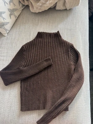 Brun ribbstickad polotröja - Mysig brun ribbstickad polotröja med lång ärm och hög hals. Tröjan har en rak passform och är tillverkad i ett mjukt material som passar perfekt till höst och vinter.Köpte tröjan på plick, lappen på tröjan är bort klippt med storlek, men hen jag köpte ifrån hade skrivit S, och de håller jag med om. 