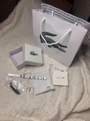Silverfärgat armband från Lacoste - Snyggt armband i silverfärgad metall från Lacoste med stilren design och diskret logga. Kommer med originalpåse, ask och papper. Perfekt accessoar för dig som gillar klassisk och modern stil.