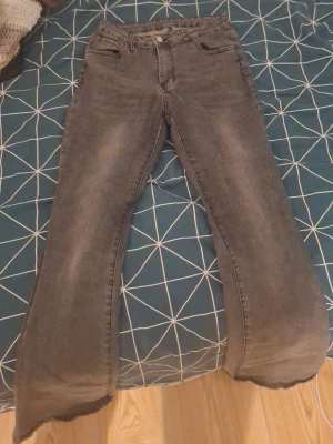 Grå bootcut jeans med slitningar - Säljer ett par grå bootcut jeans med lätt slitna detaljer och klassisk femficksmodell. Jeansen har hög midja och vida ben som ger en retrovibe. Materialet är denim med en mjuk känsla. Perfekta för dig som gillar en avslappnad men trendig stil.