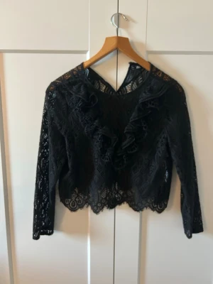 Svart spetsblus från ZARA - Säljer en elegant svart spetsblus från ZARA i storlek M. Blusen har fina spetsdetaljer, volanger framtill och långa ärmar. Perfekt till fest eller som en snygg detalj i vardagslooken. Använd men i mycket fint skick.