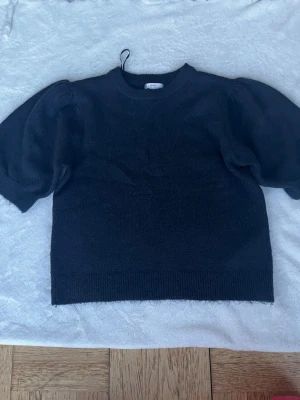 Marinblå stickad tröja med puffärm - Snygg marinblå stickad tröja med puffiga korta ärmar och rund halsringning. Tröjan har ribbade muddar vid ärmslut och nederkant, vilket ger en stilren look. Oanvänd utan prislapp.