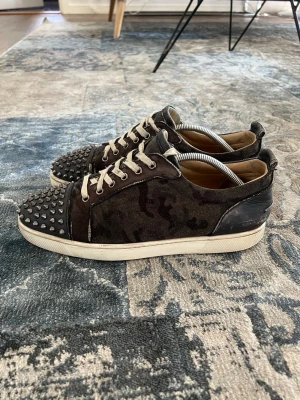 Skor med spikar i camoflauge  - Christian Louboutin sneakers, skicket går o diskutera två små håll på sidan av ena skon och några spikar har låsnat och resten är historia, storlek 43, men fortfarande väldigt stillrena på fötterna unik modell! 