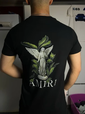 AMIRI svart T-shirt med ängelmotiv - Svart AMIRI T-shirt med elegant ängel- och blomtryck framtill samt stort motiv på ryggen. Stilren design, bekväm passform och i mycket fint skick.