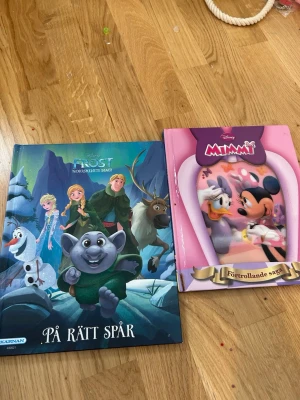 Disney Frost & Mimmi sagoböcker - Två färgglada barnböcker: en Frost-bok med karaktärer som Elsa, Anna och Olaf i blå och gröna toner, samt en rosa Mimmi-bok med Mimmi och Kajsa. Perfekta för dig som gillar magiska äventyr och klassiska Disney-figurer.