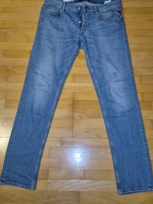 Blå raka jeans med knappgylf - Säljer ett par klassiska blå jeans med raka ben och knappgylf. Jeansen har fem fickor och är tillverkade i ett mjukt denimtyg. Perfekta för en avslappnad och stilren look.