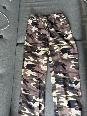 Camo mjukisbyxor med dragsko - Säljer ett par mjukisbyxor med camouflagemönster i beige, brunt och svart. Byxorna har rak passform, resår i midjan och dragsko för skön passform. Perfekta för chill dagar eller streetwear-stil. Baggy 