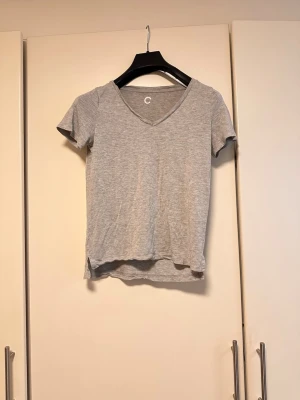 Grå v-ringad t-shirt - En enkel och stilren grå t-shirt med v-ringning och korta ärmar. Tillverkad i mjuk bomull som känns skön mot huden. Perfekt basplagg till alla outfits och lätt att matcha med andra plagg.