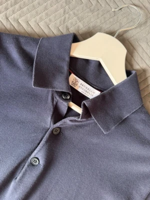 Mörkblå långärmad polotopp Brunello Cucinelli - Brunello Cucinelli – mörkblå polotröja, strl 50/M  Klassisk mörkblå långärmad polotröja från exklusiva Brunello Cucinelli. Stilren modell med krage och knappar framtill, tillverkad i ett mjukt och behagligt material som ger en elegant men avslappnad look.  • Storlek: 50/M • Färg: Mörkblå • Made in Italy • Skick: 9/10 • Nypris: ca 10 000 kr