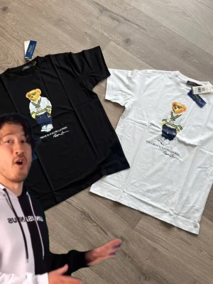 T-shirt med björntryck i svart och vitt - Två t-shirts i svart och vitt med ett stort tryck av en björn i preppy outfit på framsidan. T-shirtsen har rund hals och korta ärmar. Perfekt för dig som gillar streetwear och vill sticka ut med ett coolt motiv. OBS svarar inte på skambud då jag anser de dunder pris för 2 T-shirts 