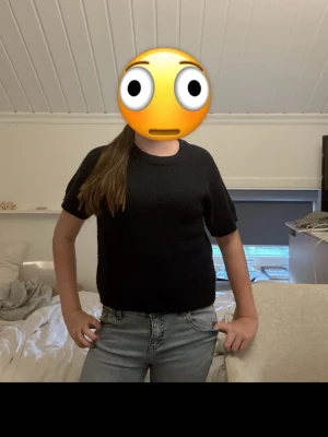 Svart stickad kortärmad tröja - En svart stickad tröja med korta ärmar och rund hals. Tröjan har en enkel och stilren design som passar perfekt till jeans eller kjol. Materialet ser mjukt och bekvämt ut, vilket gör den skön att bära hela dagen.