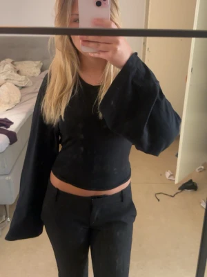 Svart långärmad topp med vida ärmar - En svart långärmad topp med riktigt vida ärmar och tight passform i midjan. Toppen är enkel men ändå trendig och passar perfekt till både jeans och kostymbyxor. Materialet ser ut att vara bomull eller polyester.