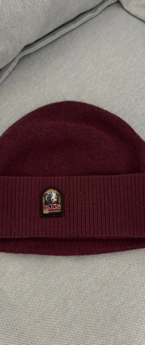 Vinröd mössa från Parajumpers - Snygg vinröd mössa från Parajumpers med uppvikt kant och klassisk logopatch framtill. Stickad i mjukt material som håller dig varm under kalla dagar. Perfekt accessoar för att lyfta din höst- och vinterstil.