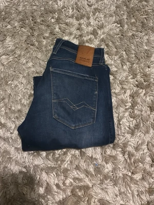 Replay jeans  - Säljer ett par mörkblå jeans från Replay med slitningar och trasiga detaljer på benen. Jeansen har klassisk femficksmodell, kontrastsömmar och en brun läderpatch bak i midjan. Perfekta för en avslappnad och trendig look.