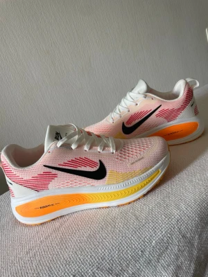Nike - Säljer ett par Nike ZoomX sneakers i vitt med rosa, orange och gula detaljer samt svart swoosh. Skorna har en luftig mesh-överdel och en tjock, färgglad sula som ger grym komfort. Perfekta för dig som vill sticka ut med dina sneakers!