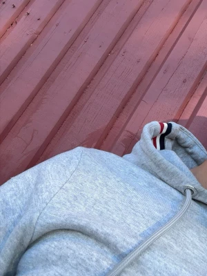 Grå Moncler hoodie storlek 3/L - Snygg grå hoodie från Moncler med dragkedja framtill och huva. Har fickor på sidorna och Moncler-logga på ärmen. Muddarna har röd, vit och marinblå rand. Perfekt för en chill och stilren look.
