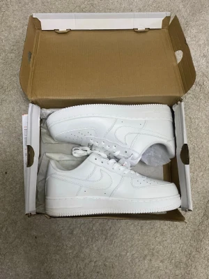 Airforce 1 Nike - Säljer ett par helvita sneakers med klassisk siluett och perforerade detaljer på tån. Skorna har en låg profil, vita skosnören och sula samt är tillverkade i slätt läder. Perfekta för dig som gillar en clean och stilren look.