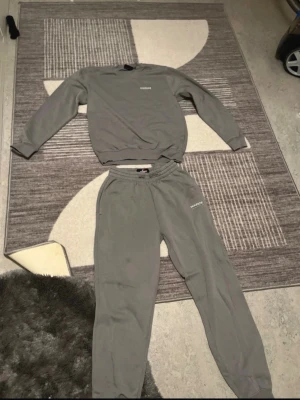 Grått loungewear-set med tryck - Mysigt grått loungewear-set med sweatshirt och matchande byxor. Båda delarna har en relaxed fit och byxorna har resår i midjan samt muddar vid bensluten. Diskret tryck på bröstet och benet. Perfekt för chill dagar hemma.