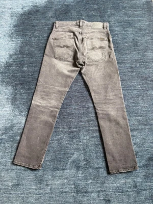 Nudie Jeans Grim Tim - Snygga grå slim fit jeans med klassisk femficksdesign och raka ben. Storlek W31 L30. Jeansen har subtila slitningar och tonade sömmar för en avslappnad look.