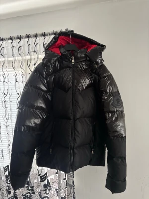 Moncler svart dunjacka med röd huva - Säljer denna riktigt snygga Moncler-jacka i svart med en grym röd insida som verkligen sticker ut. Jackan har en stilren design, blank finish på detaljerna och flera praktiska fickor med dragkedja.  ✅ Svart utsida med röd insida ✅ Moncler-detaljer ✅ Varm och perfekt för höst/vinter ✅ Snygg och unik design ✅ Pris: 2999 kr  En riktigt fin jacka för dig som vill ha något som både ser exklusivt ut och sticker ut från mängden. Passa på – först till kvarn