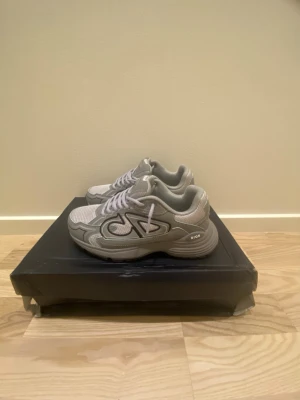 Gråa sneakers - Snygga grå sneakers med en mix av mesh och skinnpaneler. Skorna har gråa snören och en chunky sula för en modern look. Sidan pryds av en stor logga och detaljer i olika grå nyanser. Perfekta för dig som gillar streetwear och sportig stil. De är endast testade och använda en gång. Jättefräscha, storlek 37 men passar även 37,5. Tveka inte att skriva vid frågor, funderingar eller vid önskan av fler bilder. 