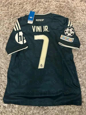 Real Madrid bortatröja, Vini Jr, 7 - Snygg mörkblå Real Madrid matchtröja med VINI JR. och nummer 7 på ryggen. Tröjan är helt ny i storlek S med Champions legue loggan på axeln.