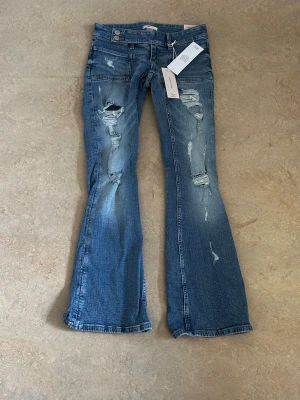 Blå bootcut jeans med slitningar - Snygga blå bootcut jeans med slitna detaljer och hål på framsidan. Baksidan har två fickor dekorerade med stjärnor i nitar. Har endast testats säljer så dem var för korta 