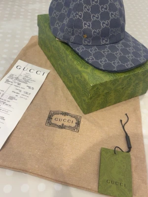 Blå GG Supreme keps från Gucci - Säljer en blå keps från Gucci i GG Supreme-mönster. Kepsen har böjd skärm och är tillverkad i canvas med all-over logotyptryck. Kommer med originalkartong, dustbag och tagg. Perfekt för dig som vill ha en lyxig och trendig accessoar.