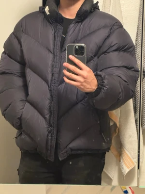 Svart vintage dunjacka från The North Face - Säljer en svart dunjacka från The North Face med dragkedja, hög krage och två sidofickor med dragkedja. Jackan har en puffig design och synliga sömmar i ett diagonalt mönster. Perfekt för kalla vinterdagar.
