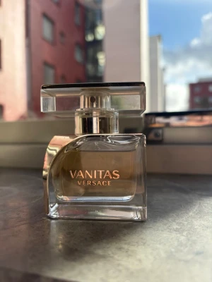 Vanitas parfym från Versace - Vanitas från Versace är en elegant parfym i en transparent glasflaska med guldfärgad spray och detaljer. Flaskan har en modern, fyrkantig form och ett stilrent lock. Doften är lyxig och flaskan känns exklusiv och trendig – perfekt för dig som gillar designerparfymer.