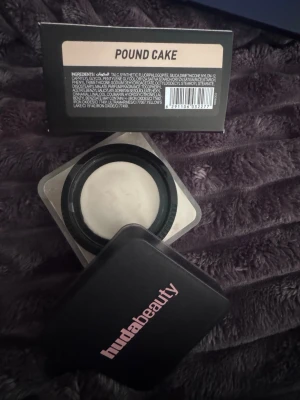 Huda Beauty Easy Bake Pound Cake puder - Huda Beauty Easy Bake Loose Baking & Setting Powder i nyansen Pound Cake. Ett löspuder i en fyrkantig svart burk med rosa logga, perfekt för att fixera makeup och ge en matt finish. Färgen är ljus och passar för att ljusa upp ansiktet.