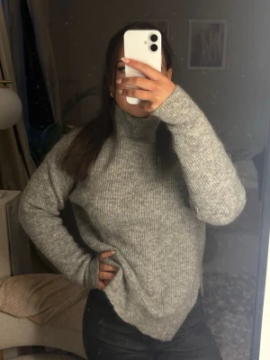 Grå stickad polotröja - Mysig grå stickad polotröja med lång ärm och ribbad struktur. Tröjan har hög krage och slitsar på sidorna vilket ger en avslappnad och trendig look. Perfekt att styla med jeans eller kjol för en chill vibe.