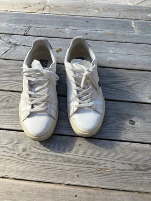 Vita veja Vega sneakers - Snygga vita sneakers från Veja med klassisk låg profil och vita skosnören. Skorna har en diskret V-logga på sidan och är tillverkade i slätt läder. Perfekta för en clean och stilren look.