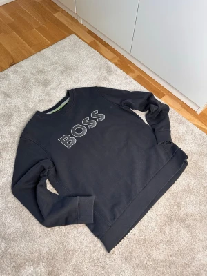 Svart sweatshirt från BOSS - Svart sweatshirt med rund hals och stora BOSS-bokstäver broderade framtill. Tröjan är i storlek L och passar dig från 170-185. Tröjan har en avslappnad passform. Perfekt för en stilren och enkel look. Skriv vid intresse och pris kan diskuteras🔥🔥🔥