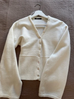 Vit kofta från Gina Tricot - Säljer en krämvit kofta från Gina Tricot i storlek XS. Koftan har v-ringning, ribbstickad midja och knappar framtill. Materialet är mjukt och ger en mysig känsla. Perfekt att slänga över en topp för en enkel och snygg look. Aldrig använd 