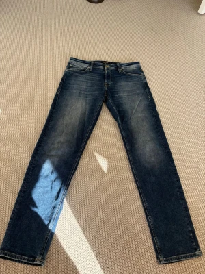 Blå jeans från Jack & Jones - Snygga blå jeans från Jack & Jones med klassisk femficksmodell och raka ben. Jeansen har en lätt tvättad look med slitningar på låren och gylf med knapp. Perfekta till vardags för en avslappnad stil.