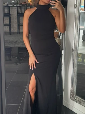 Svart långklänning med slits - Säljer en svart långklänning med hög hals och smala axelband. Klänningen har en figurnära passform och en snygg slits framtill som ger en elegant look. Perfekt för dig som vill ha en stilren och trendig outfit. Använd endast en gång! 