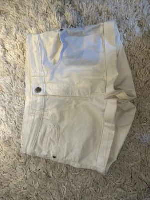 Vita höga shorts i bomull - Snygga vita shorts med hög midja och klassisk femficksdesign. Tillverkade i mjuk bomull med knapp och dragkedja framtill. Perfekta för varma dagar och enkla att matcha med olika toppar.