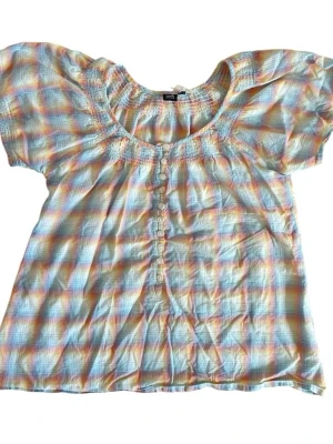 Rutig blus  - Rutig blus i regnbågsfärger med puffärm 💛  Storlek okänd, uppskattad storlek S.  Märke: Soda.  Modellen har storlek XS–S och är 167 cm lång.     Observera att alla plagg är second hand och därför kan ha mindre tecken på användning; eventuellt tydligare slitage anges i beskrivningen.