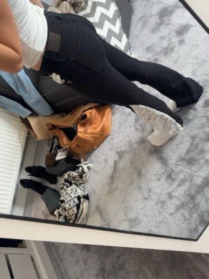 Svarta jeans med spetsdetalj - Unika svarta jeans med utsvängda ben och vit spetsdetalj längs ena benet. Jeansen har låg midja, bakfickor och dekorativa sömmar. Perfekta för dig som vill sticka ut med din stil!