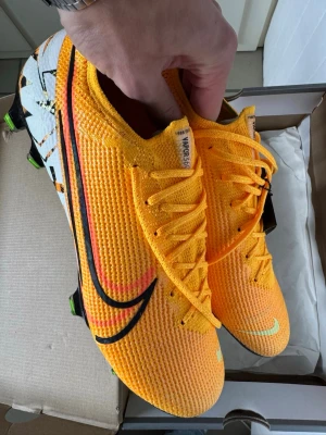  NIKE MERCURIAL VAPOR 13 ELITE FG - ORANGE/SVART LIMITED EDITION - Ej använda. Limiterade fotbollsskor par 1988/2019 stycken. Storlek EU 46. köpta på unisportstore. Hör av dig om du har några frågor😊