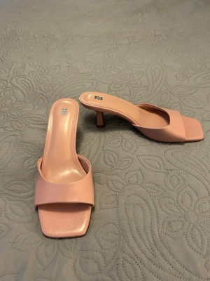 Ljusa rosa slip-in pumps från Pull & Bear med låg klack - Snygga slip-in pumps i ljusrosa från Pull & Bear med fyrkantig tå och låg klack. Skorna har bred rem över foten och är tillverkade i ett glansigt material som ser ut som konstläder.