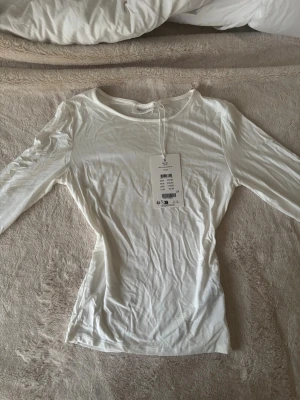 Vit långärmad topp från Signature - Säljer en enkel och stilren vit långärmad topp från Signature. Toppen har en rund halsringning och är figurnära i modellen. Perfekt att styla med jeans eller kjol för en clean look.