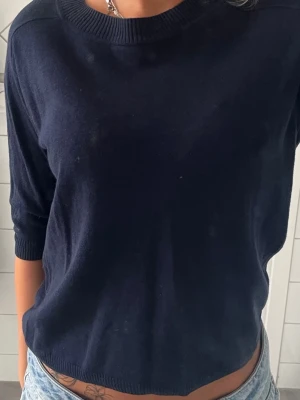 Mörkblå basic tröja med 3/4-ärm - En enkel och stilren mörkblå tröja med 3/4-ärm och rund halsringning. Tröjan har ribbade muddar vid ärmslut och hals, och är gjord i ett mjukt, tunt material som passar perfekt till jeans eller kjol.