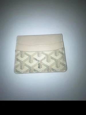 Beige kortfodral med mönster - Snyggt beige kortfodral med klassiskt grafiskt mönster och flera kortfack. Tillverkat i läder med detaljer i ljust beige och grått. Perfekt för att hålla koll på dina kort på ett stilrent sätt.