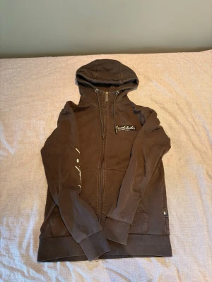 Hoodrich tracksuit svart - Säljer en svart hoodie från Hoodrich med dragkedja framtill, huva med snörning och vita tryckdetaljer på bröstet, ryggen och ena ärmen. Hoodien har långa ärmar och ribbade muddar. Perfekt för en chill och street-inspirerad look.