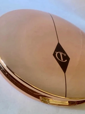 Charlotte Tilbury puderfoundation - Snygg puderfoundation från Charlotte Tilbury i en lyxig, oval guldig dosa med spegel. Färgen är ljusbeige och formulan är pressad puder, perfekt för en naturlig finish. Dosan har märkets ikoniska logga på locket.